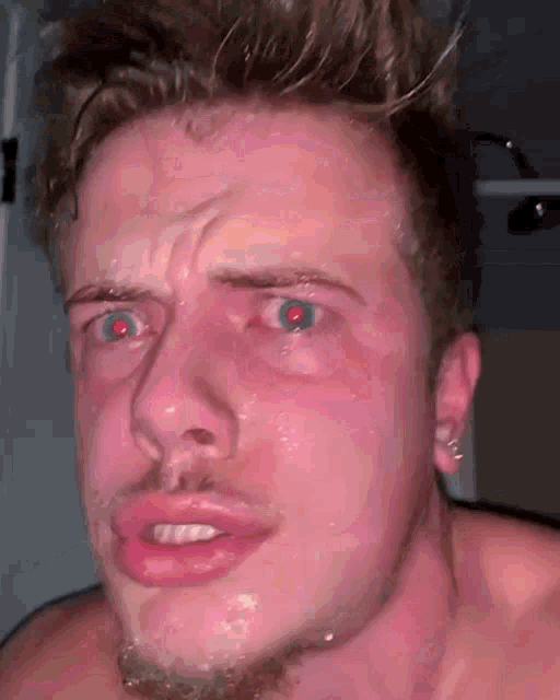 a close up of a man 's face with red eyes and a beard .