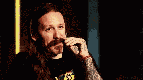 a man with long hair and a mustache has a tattoo on his arm