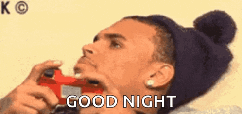 a man in a beanie is holding a video game controller in his mouth and saying `` good night '' .