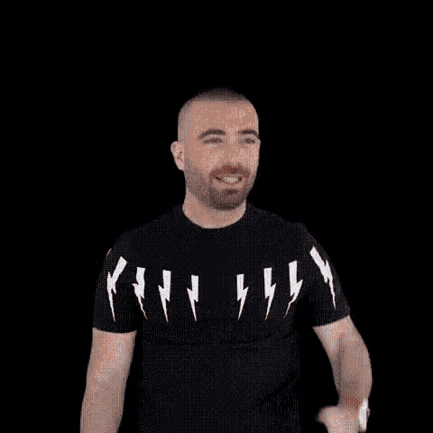 a man wearing a black t-shirt with lightning bolts on it is smiling and waving his hand .