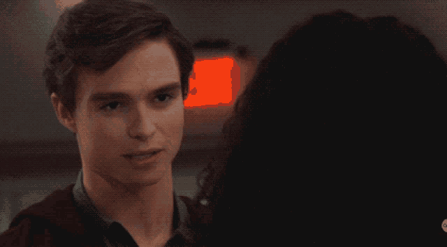 a man and a woman are looking at each other with a red exit sign in the background