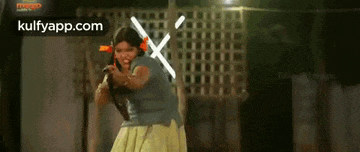a woman in a blue shirt and yellow skirt is holding a sword in front of a fence .