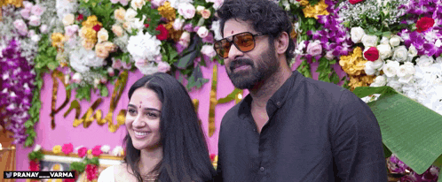 a man and a woman are posing for a picture in front of flowers and the word pranay is on the bottom