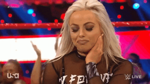 a woman with blonde hair is standing in a wrestling ring with her hand on her chin .