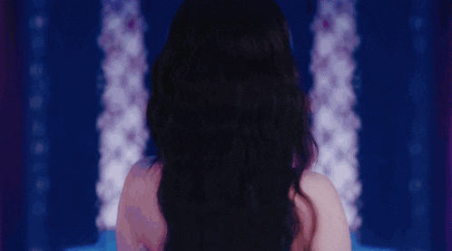 a woman with long black hair is standing in front of a purple background .