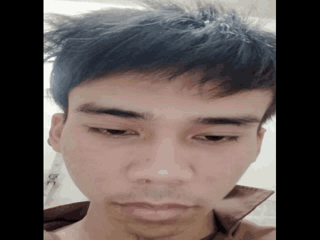 a close up of a young man 's face with a brown shirt on