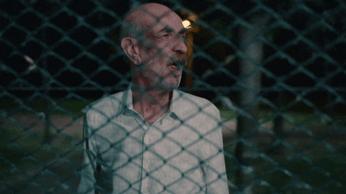 an elderly man behind a chain link fence looking out