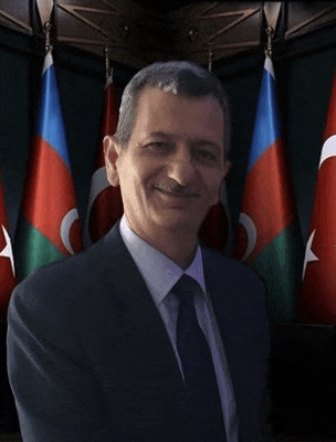 a man in a suit and tie is smiling in front of a row of flags .