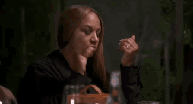 a woman with a ring on her finger is sitting at a table with her hands in the air .