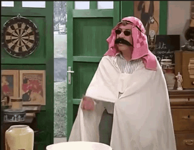 a man with a mustache and sunglasses is standing in front of a dart board .