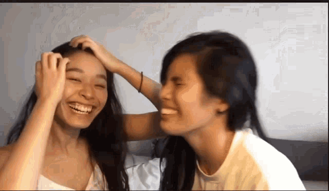two women are laughing and touching each other 's faces .