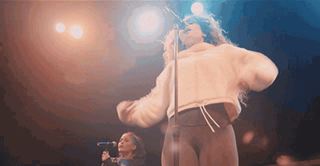 a woman singing into a microphone while another woman stands behind her