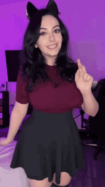 a woman wearing a cat ear headband and a black skirt is giving a thumbs up .