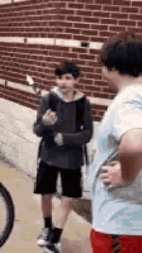 a man and a boy are standing next to each other on a sidewalk in front of a brick wall .