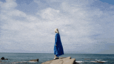 a woman in a blue dress is laying on a large rock