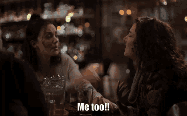 two women are sitting at a table and one of them is saying me too !