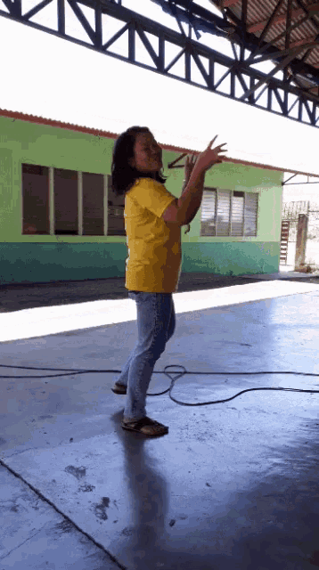 a woman in a yellow shirt stands in front of a green building with her arms outstretched
