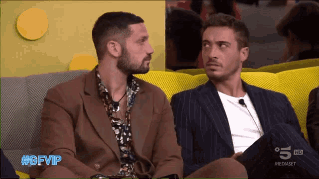 two men sitting on a yellow couch with the hashtag #gfvip on the screen