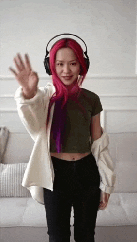 a woman with red hair and headphones is waving at the camera .