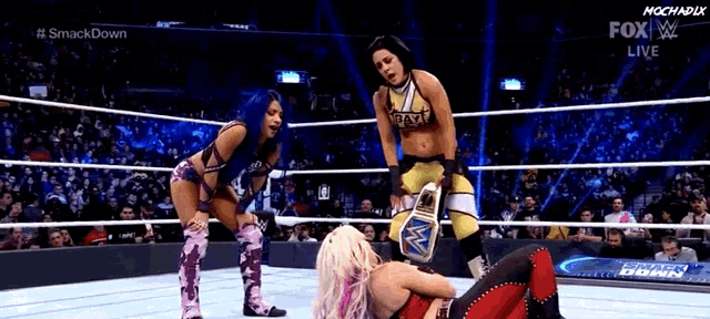 three women are wrestling in a wrestling ring and one of them is wearing a wwe championship belt .