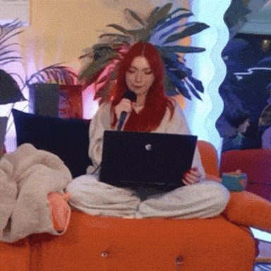 a woman with red hair is sitting on a couch with a laptop and microphone