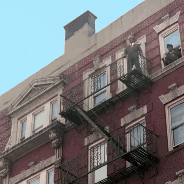 a man in a suit stands on a fire escape
