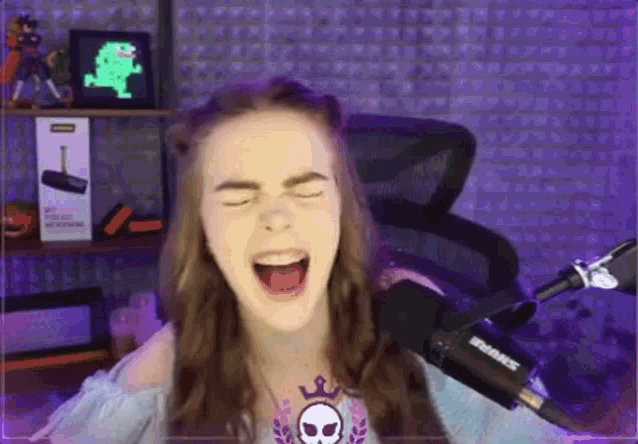 a girl is screaming into a microphone while sitting in front of a purple wall .