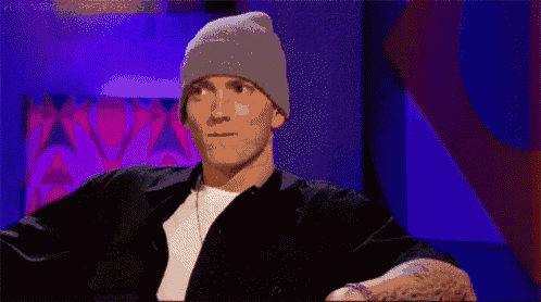 a man wearing a gray beanie and a black shirt is sitting in front of a purple wall .