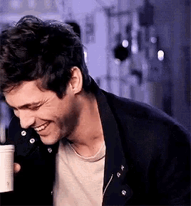 a man is smiling while holding a cup of coffee in his hand .