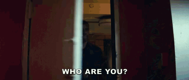 a man is standing in a doorway with the words `` who are you '' written on the screen .