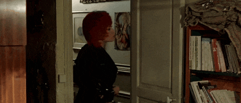 a woman with red hair is standing in a doorway next to a bookshelf with books on it