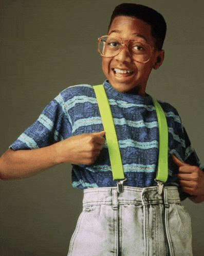 a young boy wearing glasses and suspenders points at his chest