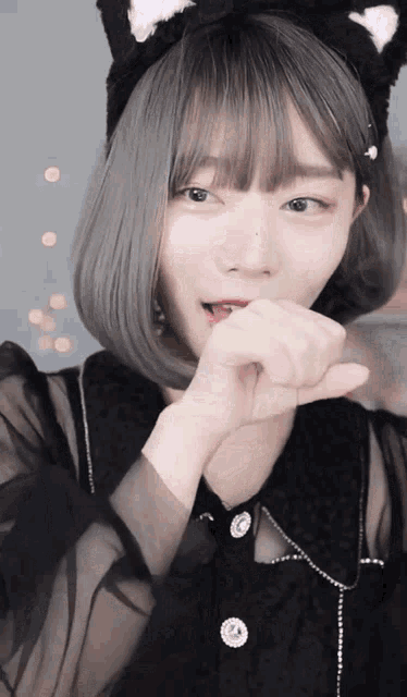 a girl wearing a black cat ear headband covering her mouth
