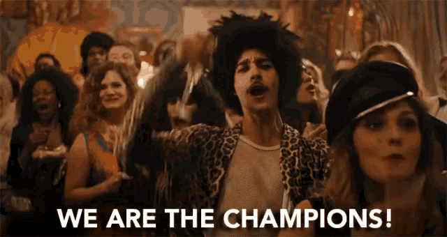 a man in a leopard print jacket stands in front of a crowd of people and says we are the champions