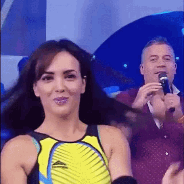 a woman in a yellow tank top is smiling while a man holds a microphone .