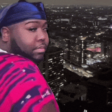 a man wearing a headband and sunglasses stands in front of a cityscape at night