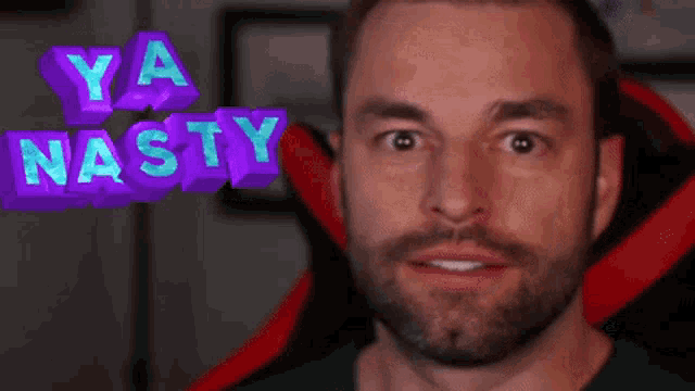 a man with a beard is sitting in a red chair with the words ya nasty above his head
