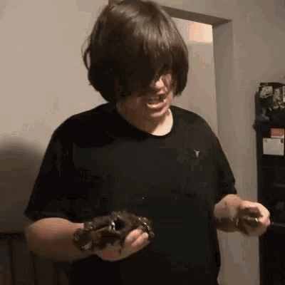 a man in a black shirt is holding a frog in his hands and making a funny face .