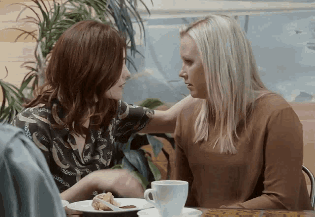 two women are sitting at a table with a plate of food and cups of coffee