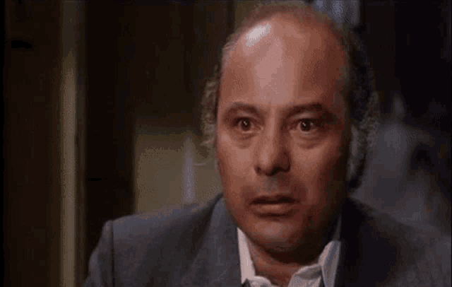 a bald man in a suit and tie is looking at the camera with a serious look on his face .