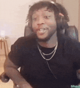 a man wearing headphones and a necklace is sitting in a chair making a funny face .