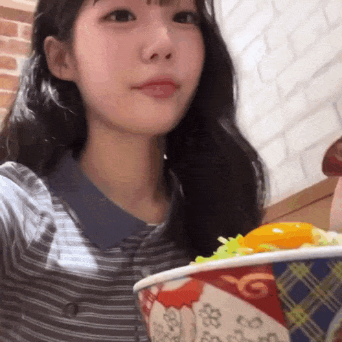 a young girl is holding a bowl of food and looking at the camera .