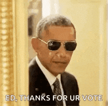 barack obama is wearing sunglasses and a suit and tie while standing in front of a picture frame .