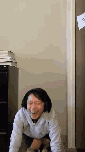 a woman wearing headphones and a grey sweatshirt is laughing