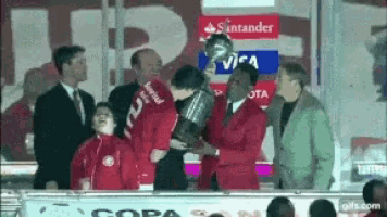 a man in a red suit is holding a trophy in front of a sign that says santander