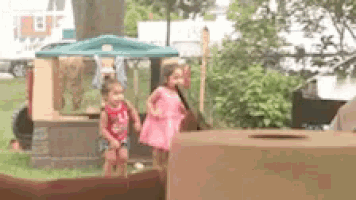 two little girls standing next to each other in front of a cardboard house .