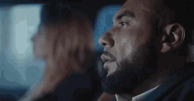a man with a beard is sitting in the back seat of a car with a woman in the background .