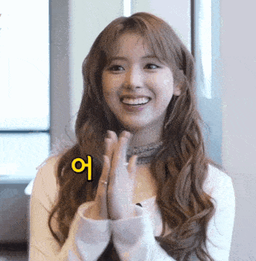 a woman with long brown hair is smiling with a yellow sign above her that says " 어 "