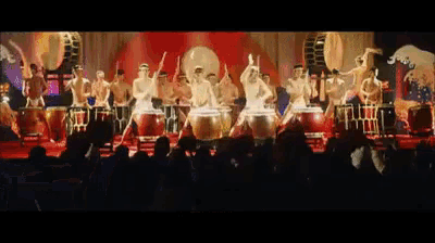 a group of men are playing drums in front of a crowd of people