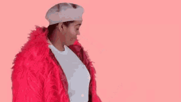 a woman wearing a pink fur coat and a white beret is waving .